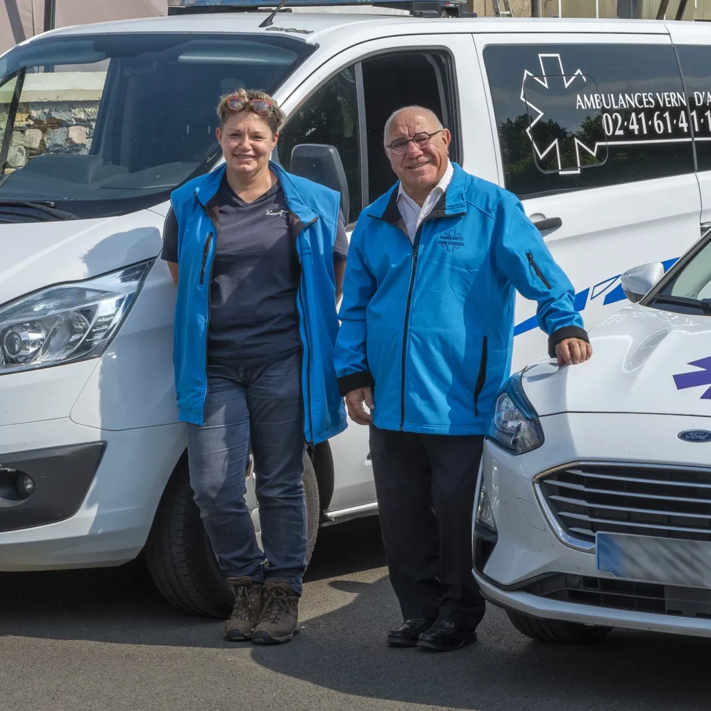 Deux ambulanciers en tenue professionnelle posant devant leurs véhicules.