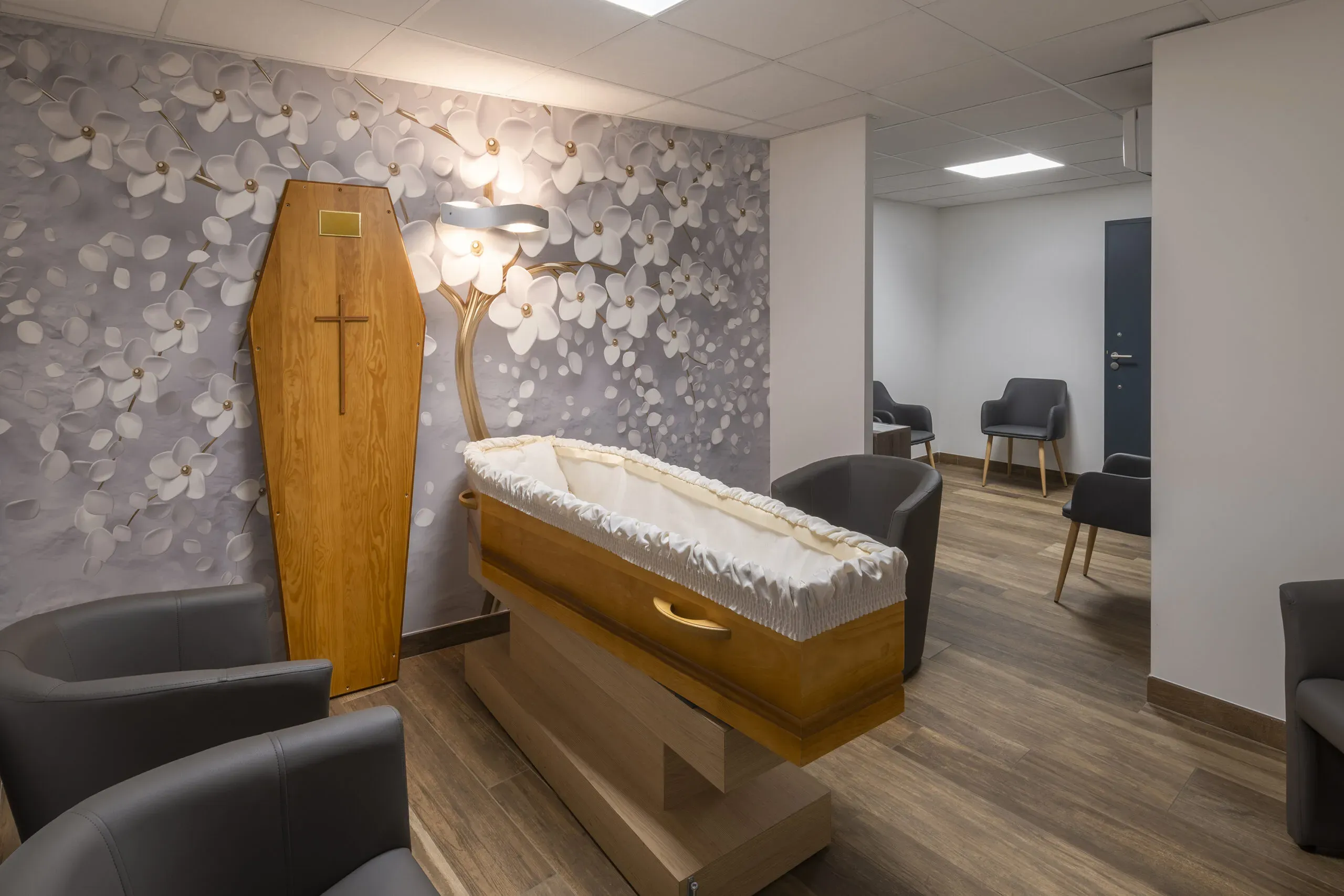 Chambre funéraire avec cercueil en bois et décoration florale murale.